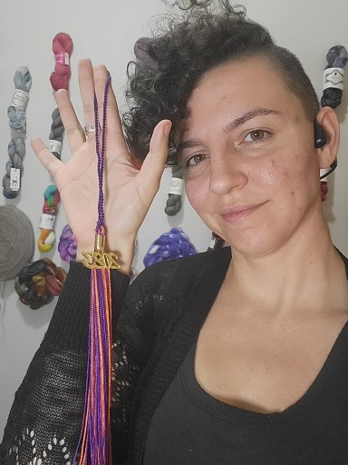 Image of Dr. Tobias holding her graduation tassel in front of a wall of yarn.